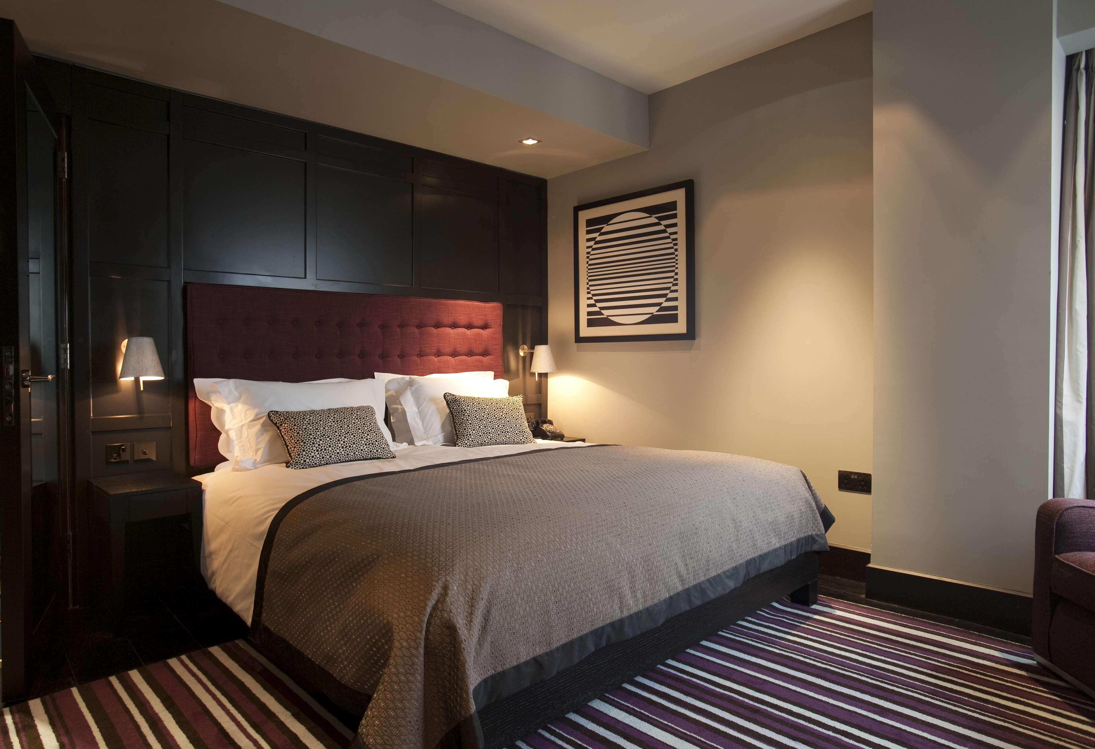 The Fitzwilliam Hotel Belfast Ngoại thất bức ảnh The photo shows a stylish and modern hotel room. It features a large bed with a tufted headboard in a deep burgundy color. The bed is dressed with neutral-toned bedding and decorative pillows. On either side of the bed, there are small bedside lamps 
