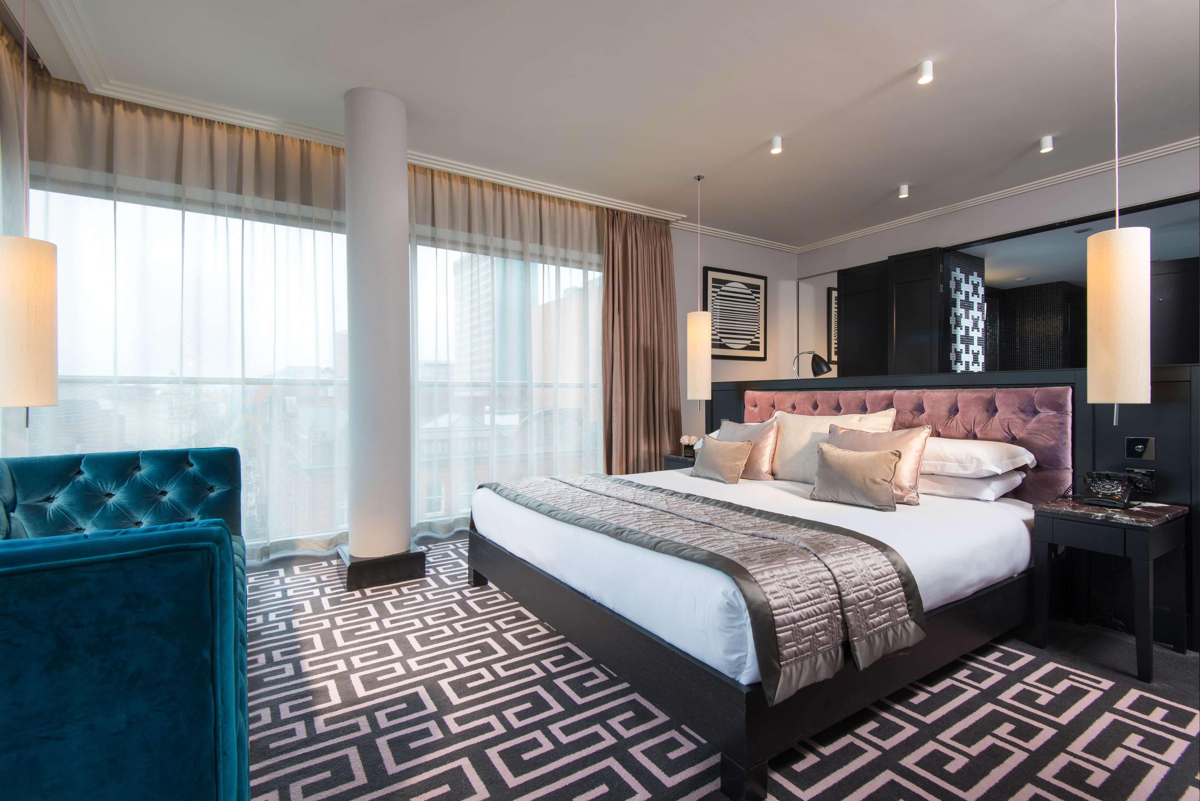 The Fitzwilliam Hotel Belfast Ngoại thất bức ảnh The photo showcases a modern hotel room. It features a large bed with plush pillows and a stylish headboard. The room has large windows with sheer curtains, allowing natural light to filter in. The floor is covered with a patterned carpet that contra